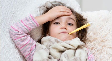 Sick child with a thermometer in her mouth. She is holding her forehead.